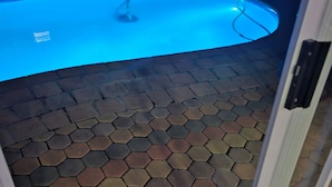 Une piscine dotée d’un sol carrelé en forme d’hexagone, d’une porte en verre et d’un paillasson carrelé à l’entrée.