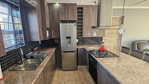 Une cuisine moderne avec des meubles de couleur bois foncé, des appareils électroménagers en acier inoxydable, une cuisinière à gaz et un four encastré.