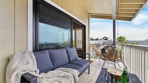 A balcony with a sofa, two wicker chairs, a table with popcorn and a bottle, and a view of buildings and trees. - Calafia Cove by Avantstay Ocean View Balcony + BBQ Walk to Beach + Downtown (San Clemente)