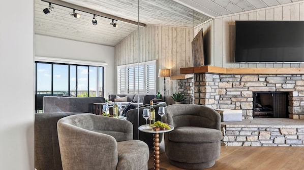 A spacious living area with a stone fireplace, modern furniture, and large windows offering a view.