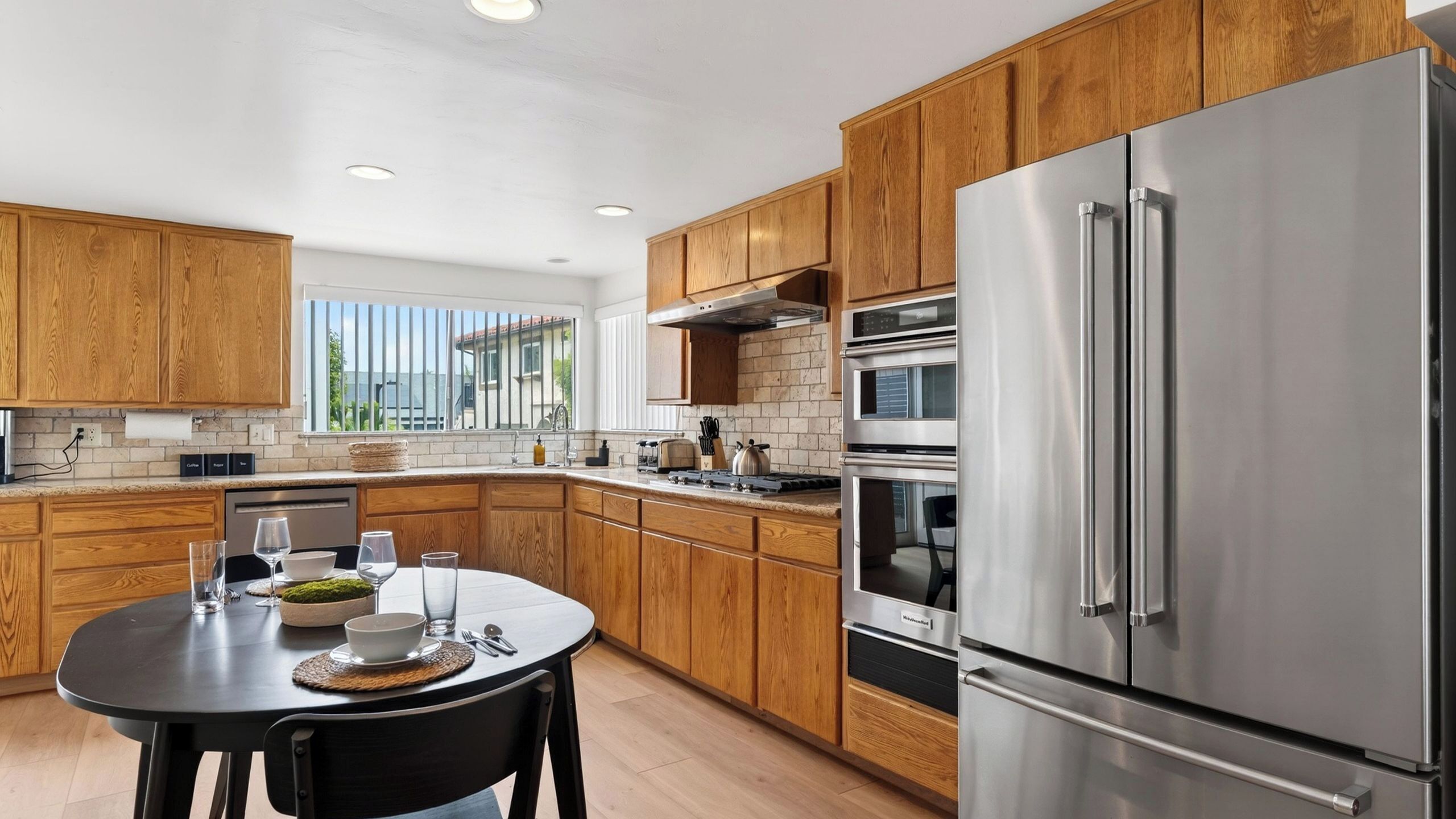 A modern kitchen with wooden cabinets, stainless steel appliances, and a dining area with a table set for two.