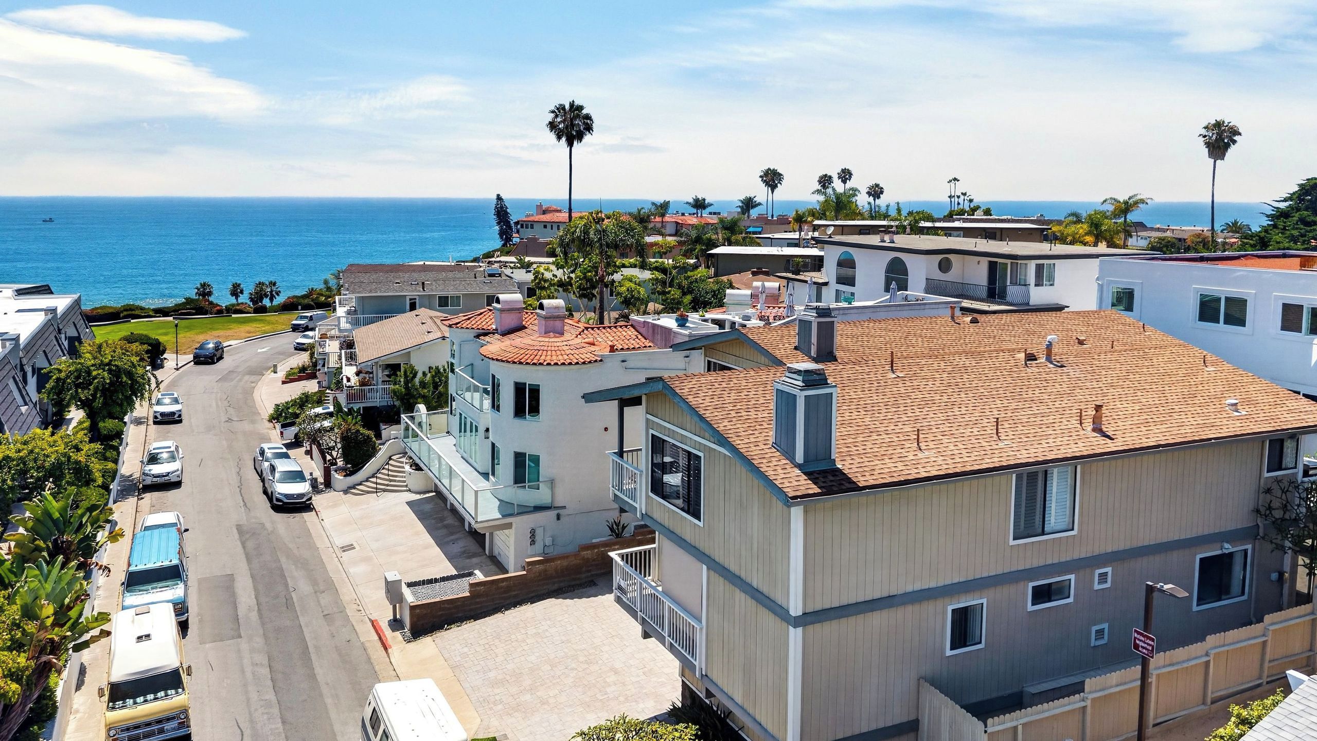 A coastal residential area with modern buildings, a clear view of the ocean, and a street with parked cars.