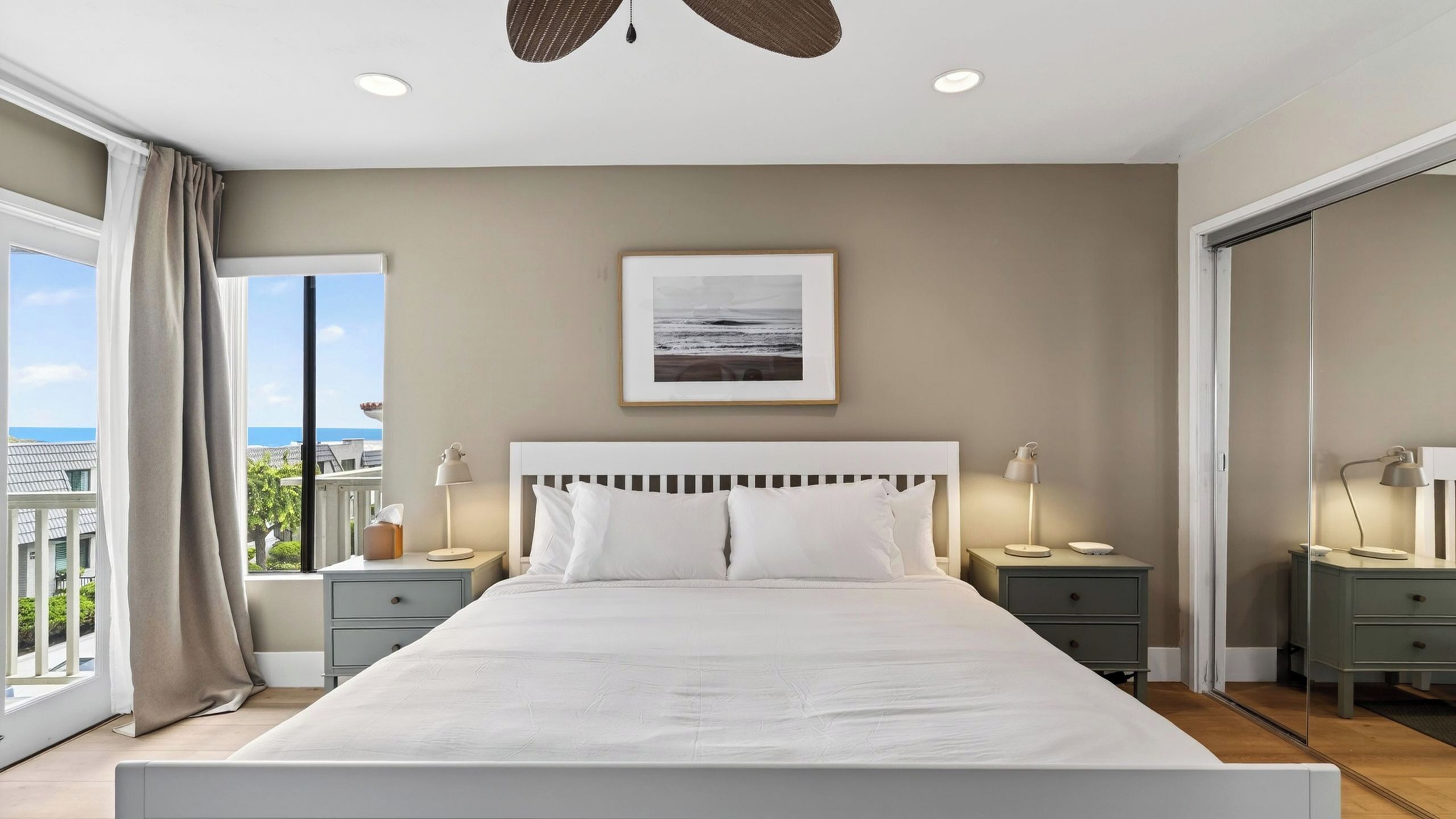 A bedroom with a large bed, two bedside tables with lamps, a framed picture on the wall, and a view through a window.