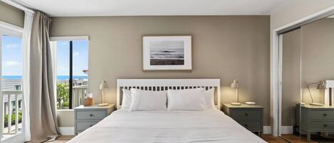 A bedroom with a large bed, two bedside tables with lamps, a framed picture on the wall, and a view through a window.