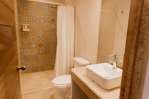 Un bagno con parete in piastrelle decorate, un water bianco, una tenda da doccia e un lavandino con specchio.