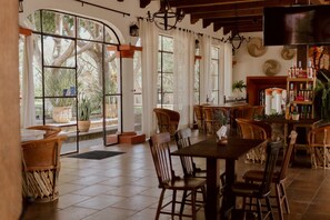 Un comedor con una mesa grande y sillas, una barra con botellas, y ventanas amplias con vistas a árboles.