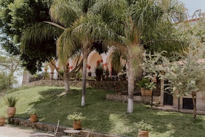 A courtyard with palm trees, a stone wall, and a building with arches. - Hacienda San Nicolas de las Fuentes  (Teuchitlán)