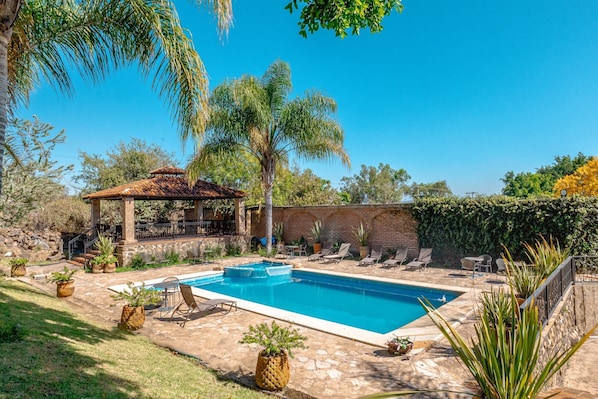 Ein Schwimmbecken mit LiegestĂŒhlen, einer Pergola und Topfpflanzen.