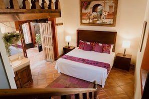 A bedroom with a bed, two bedside tables, a nightstand, a wooden staircase, a bathroom with a sink, and a door leading to another room. - Hacienda San Nicolas de las Fuentes  (Teuchitlán)