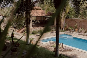 A pool area with lounge chairs, a small building with a tiled roof, and a brick wall. - Hacienda San Nicolas de las Fuentes  (Teuchitlán)