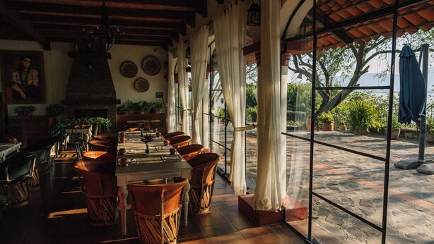 A restaurant with a long table, chairs, and a view through large windows. - Hacienda San Nicolas de las Fuentes  (Teuchitlán)