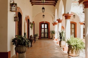 Un pasillo con arcos, plantas en macetas y faroles colgantes.