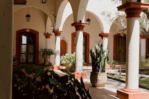 A courtyard with arches, columns, potted plants, and a fountain.