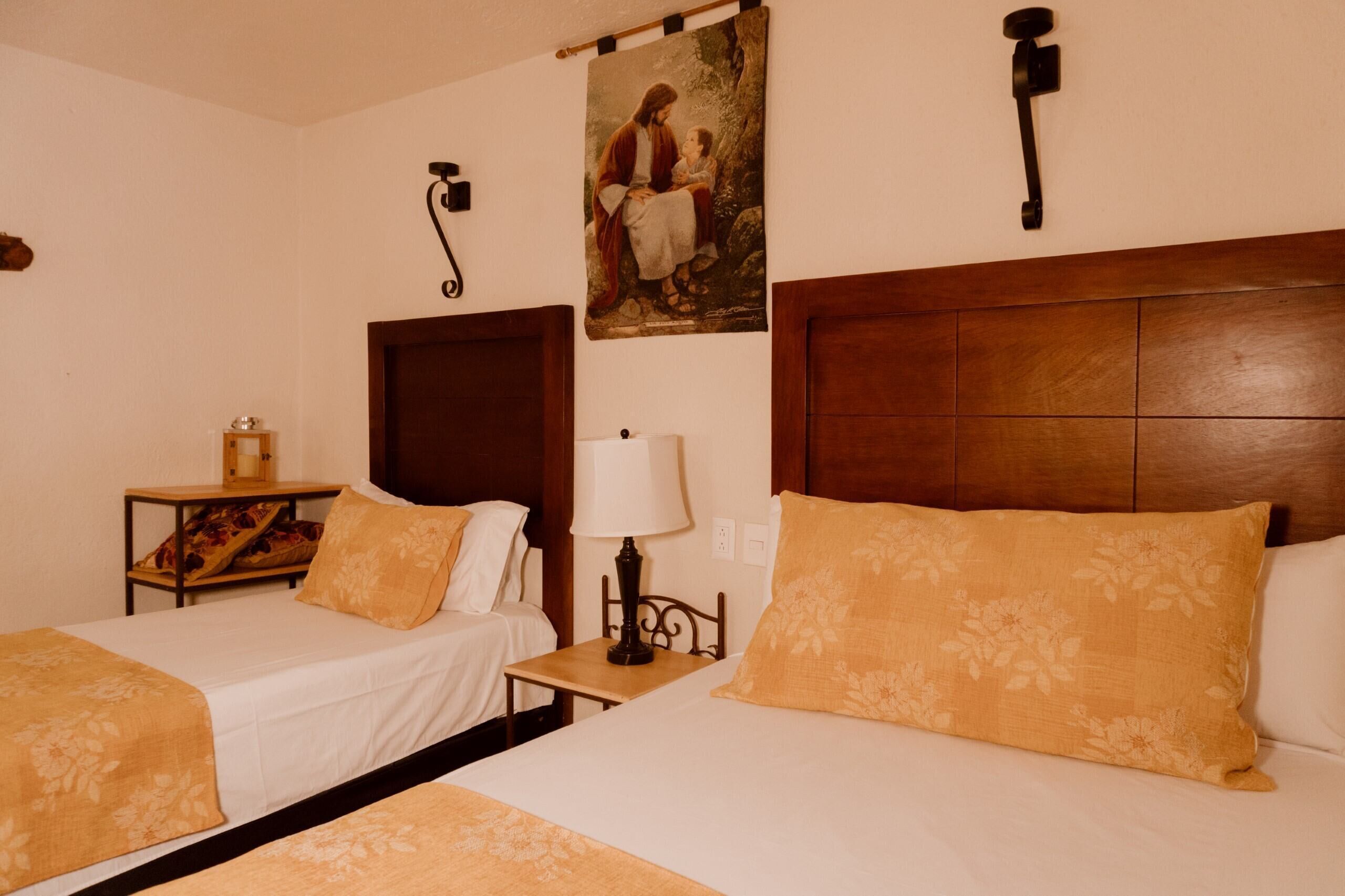 A hotel room with two beds, a wooden headboard, a nightstand with a lamp, and a wall-mounted telephone.