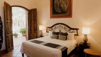 A hotel room with a bed, two bedside lamps, a painting on the wall, and an open door leading to a courtyard.