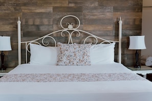 Ein Bett mit weiĂem Metallgestell, weiĂer BettwĂ€sche und einem blumigen Kopfkissen.