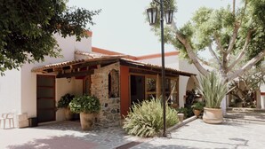 A small building with a tiled roof, stone walls, and a wooden pergola. There are potted plants and a large tree in front. - Hacienda San Nicolas de las Fuentes  (Teuchitlán)