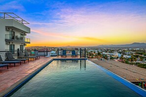 A rooftop pool with lounge chairs and a view of the city at sunset. - Loft Close to the Ocean With Rooftop Infinity Pool, Balcony & gym - Dog-friendly (Cabo San Lucas)