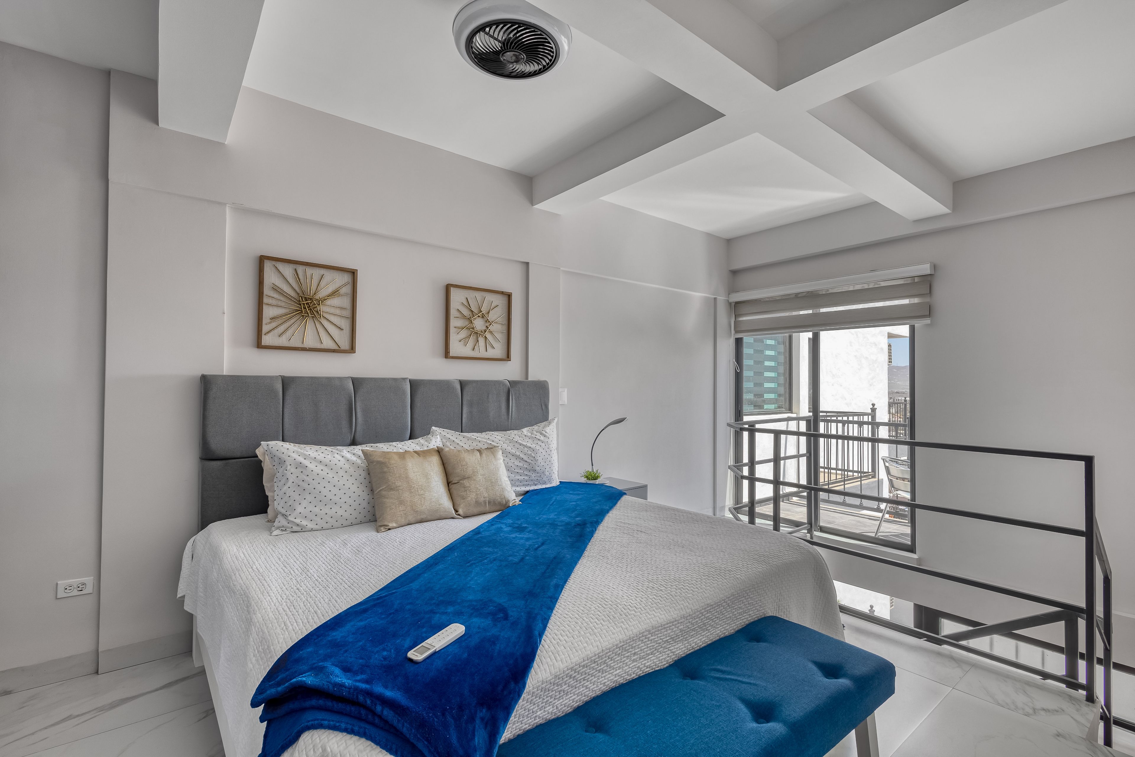 Ein modernes Schlafzimmer mit einem großen Bett, Balkonblick und Deckenventilator.