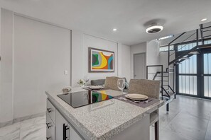 A modern kitchen with a granite countertop, a dining area with a sofa, and a staircase leading to an upper level. - Loft Close to the Ocean With Rooftop Infinity Pool, Balcony & gym - Dog-friendly (Cabo San Lucas)