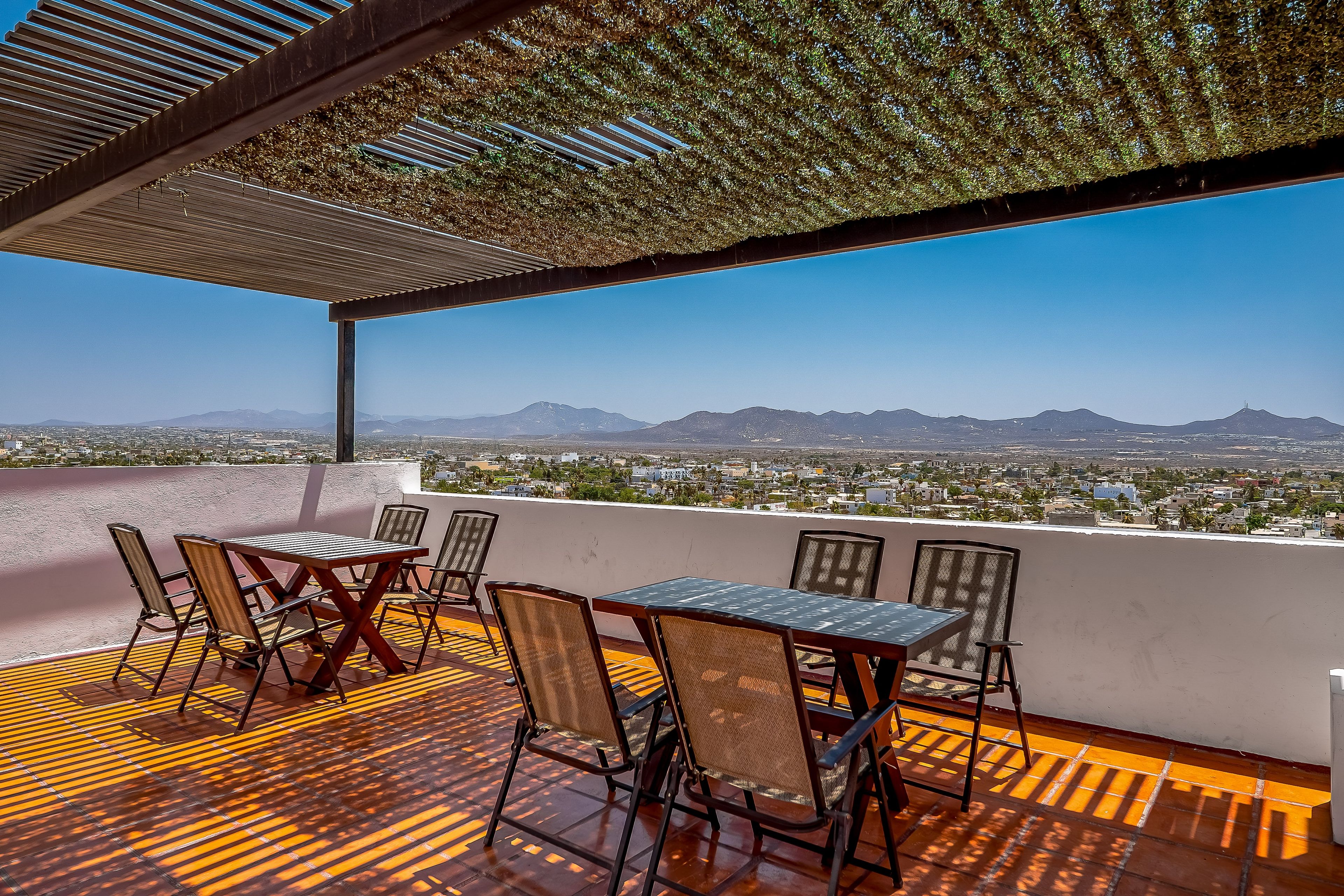A terrace with a table and chairs, a pergola, and a view of a city and mountains.