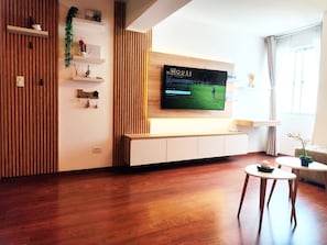 Ein modernes Wohnzimmer mit einem großen Flachbildfernseher an der Wand, Holzboden und einem minimalistischen Design.