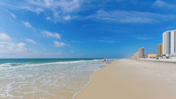 A beach with a sandy shore, ocean waves, and high-rise buildings in the background. - Steps to Beach! Heated Pool & Modern Luxury (gulf shores)
