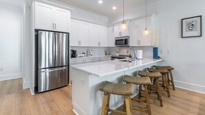 A modern kitchen with white cabinetry, stainless steel appliances, a central island with stools, and pendant lighting. - Steps to Beach! Heated Pool & Modern Luxury (gulf shores)
