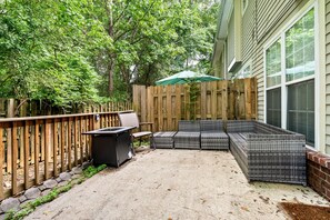 Une terrasse couverte, agrémentée d’une clôture en bois, de sièges d’extérieur et d’un parasol vert.