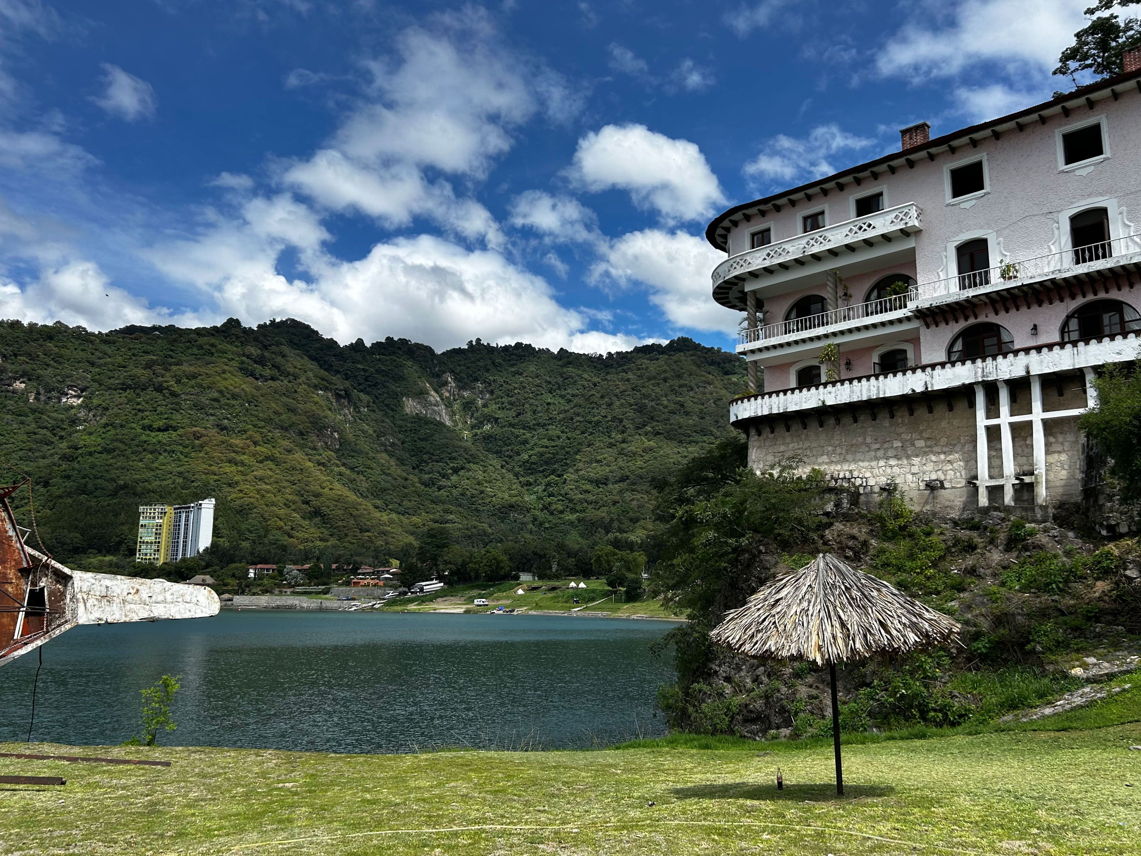 A building with balconies overlooking a lake, surrounded by greenery and hills.