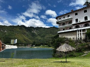 Un edificio con balcones que dan a un lago, rodeado de vegetación y colinas.