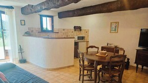 A cozy living area with a sofa, dining table, chairs, a TV, and a kitchen area with a microwave. - For nature lovers, absolute peace and quiet (Peyroules)