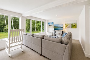A modern living room with a sectional sofa, a white rocking chair, a flat-screen TV, and artwork on the walls.