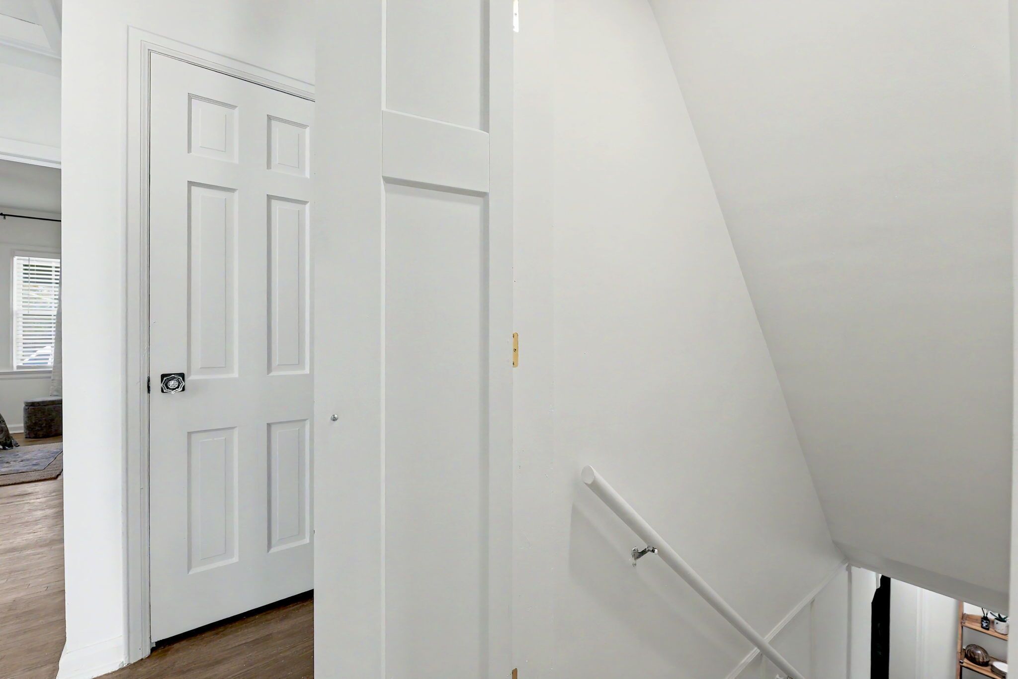 Una puerta blanca con manija, una pared blanca y una barandilla blanca.