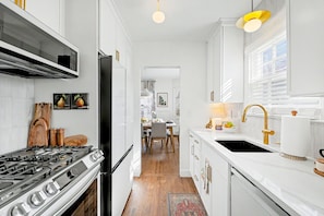 A narrow kitchen with white cabinetry, a gas stove, a black refrigerator, and a gold faucet. - Crown Heights Cutie in Perfect Location! (Wichita)