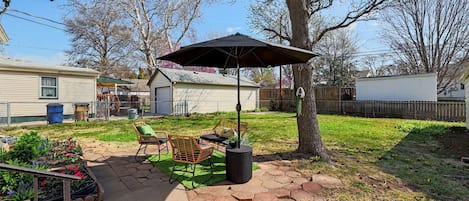 A backyard patio with hexagonal tiles, a metal table, two chairs, a trash can, and a tree.