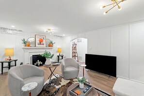 A modern living room with two armchairs, a fireplace, a flat-screen TV, and a ceiling light fixture. - Crown Heights Cutie in Perfect Location! (Wichita)