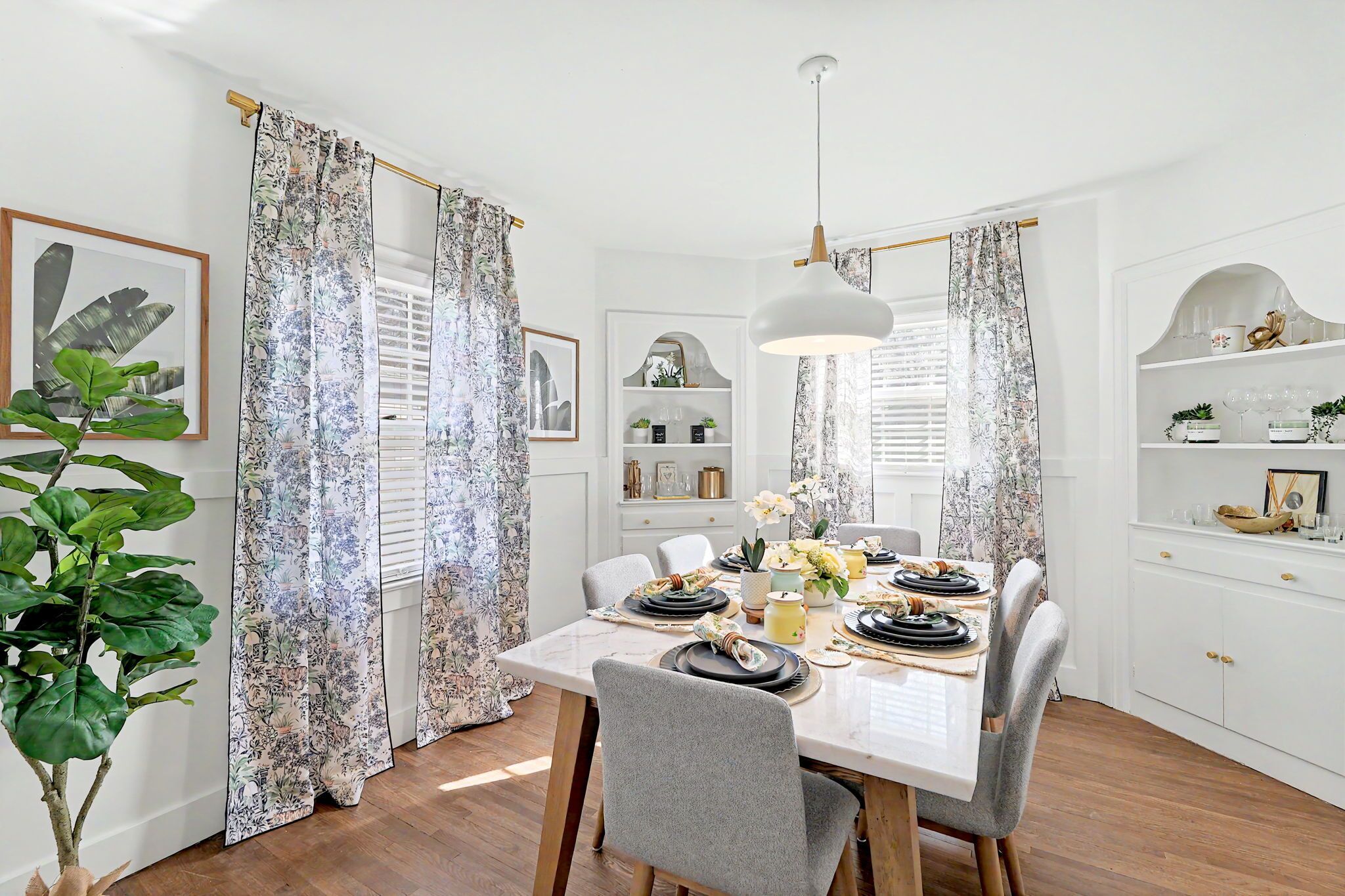 Un coin repas avec une table dressée pour quatre personnes, entourée de chaises, et un luminaire suspendu au-dessus.