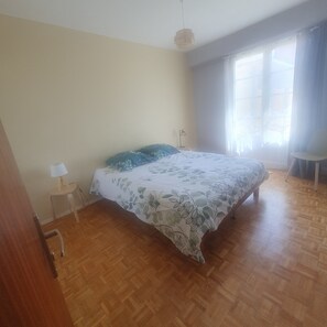 A bedroom with a bed, a nightstand, a lamp, a chair, and a window with curtains. - On the Ile d'Offard in a quiet neighborhood 10 minutes from the town center and train station (Saumur)