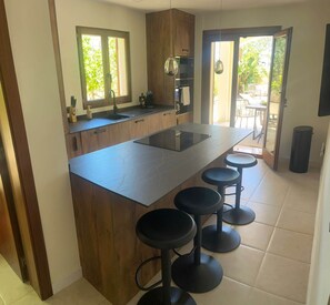 A modern kitchen with a central island, bar stools, and a view to the outdoors. - Villa Balear (Sol de Mallorca)