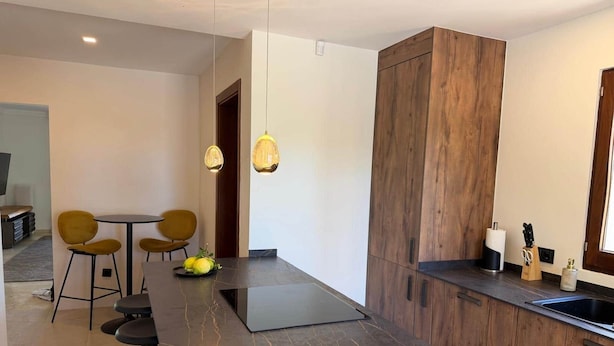 Una cocina moderna con encimera de mármol oscuro, armarios de madera y un comedor con sillas amarillas.
