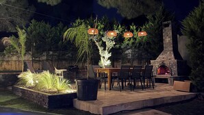 Un patio al aire libre con chimenea de piedra, mesa de comedor, sillas y faroles decorativos.