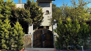 Un edificio con una torre alta, una entrada protegida por una reja y árboles circundantes.