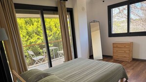 Un dormitorio con cama, cómoda, espejo y balcón con sillas.