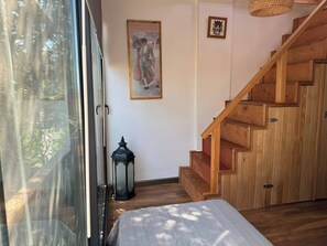 A wooden staircase, a bed, a window with a view of trees, and a wall with a framed picture and a small emblem. - Lavilla Parsdoren House (Karaburun)