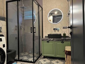 A modern bathroom with a glass-enclosed shower, a round mirror, a sink, and a green cabinet. - Lavilla Parsdoren House (Karaburun)