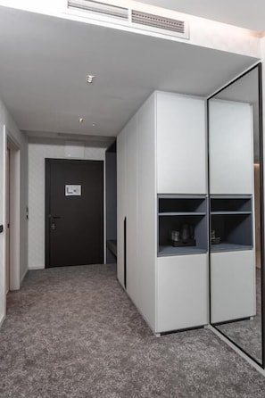 A room with a grey carpet, a door, and a white wardrobe with shelves. - Cube (Bar)