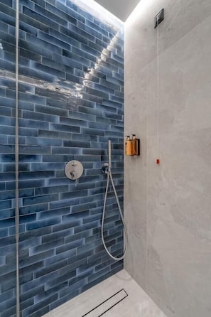 A shower with a blue-tiled wall and a plain wall on the right. - Cube (Bar)