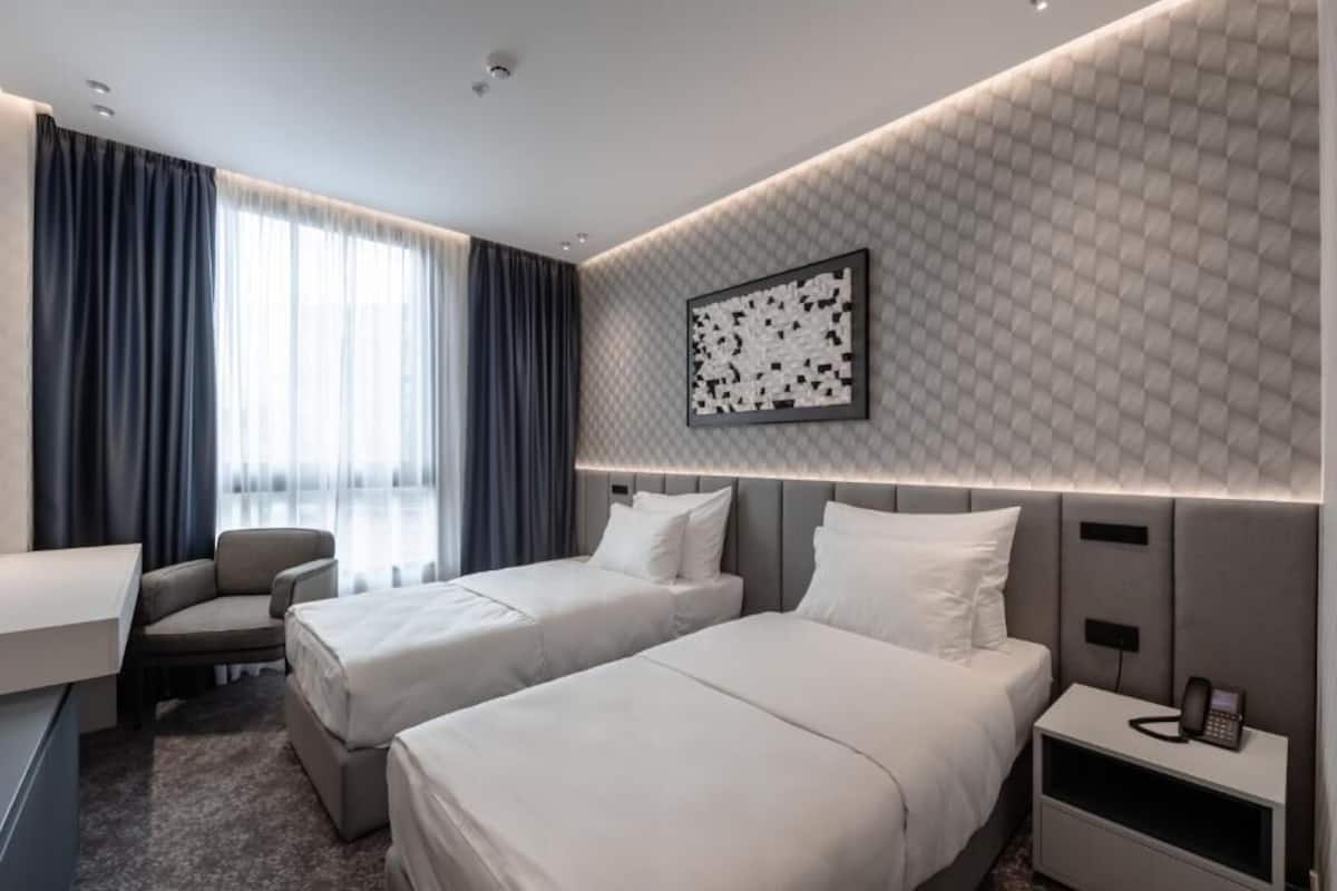 A hotel room with two beds, a desk, a chair, and a phone on the nightstand.