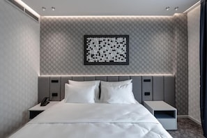 Moderni hotellihuone, jossa on suuri sänky, yöpöydät, puhelin ja seinälle kiinnitetty taideteos.